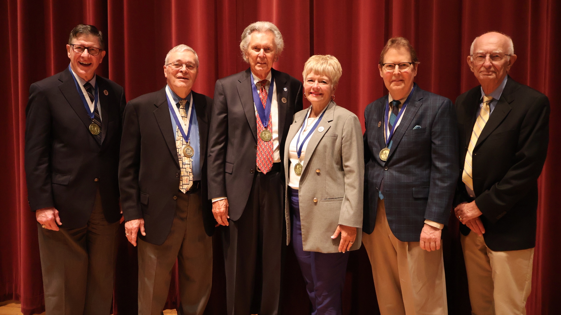 A group of past Weaver Medal of Honor recipients pose together wearing their medals on stage