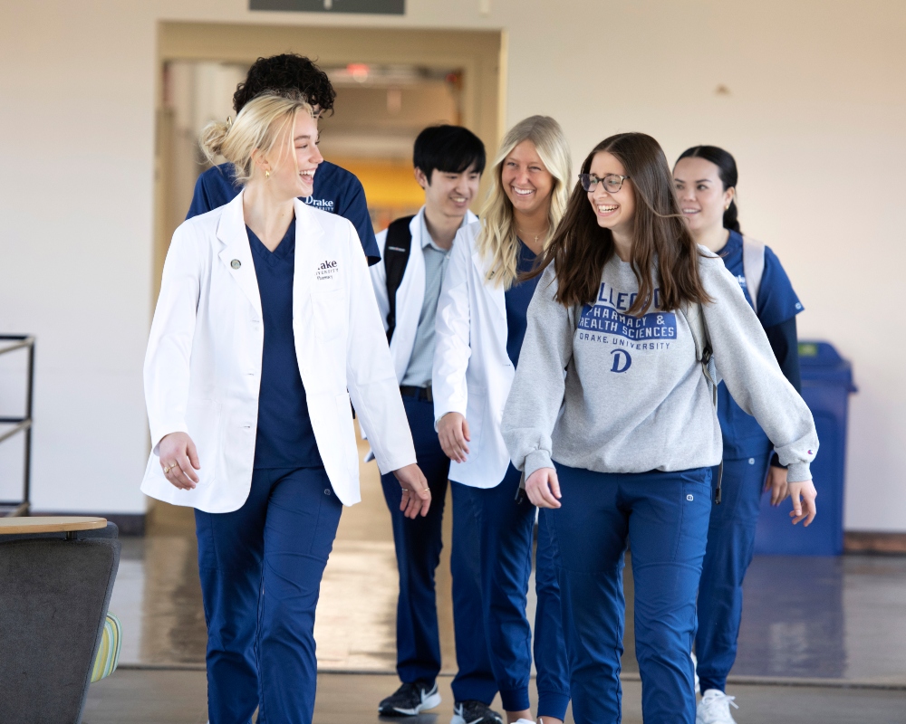 A group of students from Drake's College of Pharmacy and Health Sciences wearing sweatshirts or lab coats converse as they walk to class