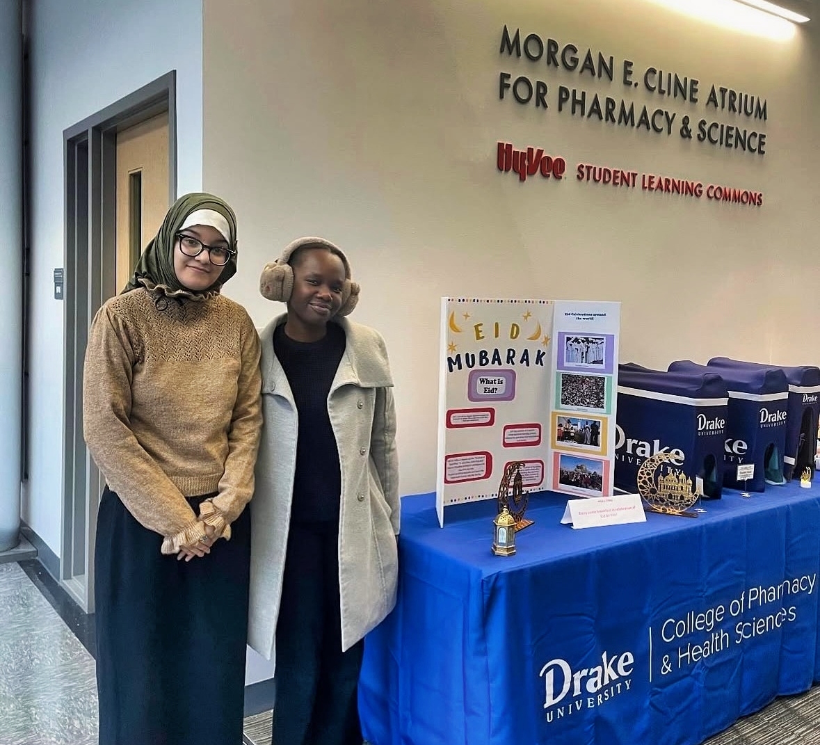 Drake students stand in front of a table with an Eid Mubarak poster and breakfast items