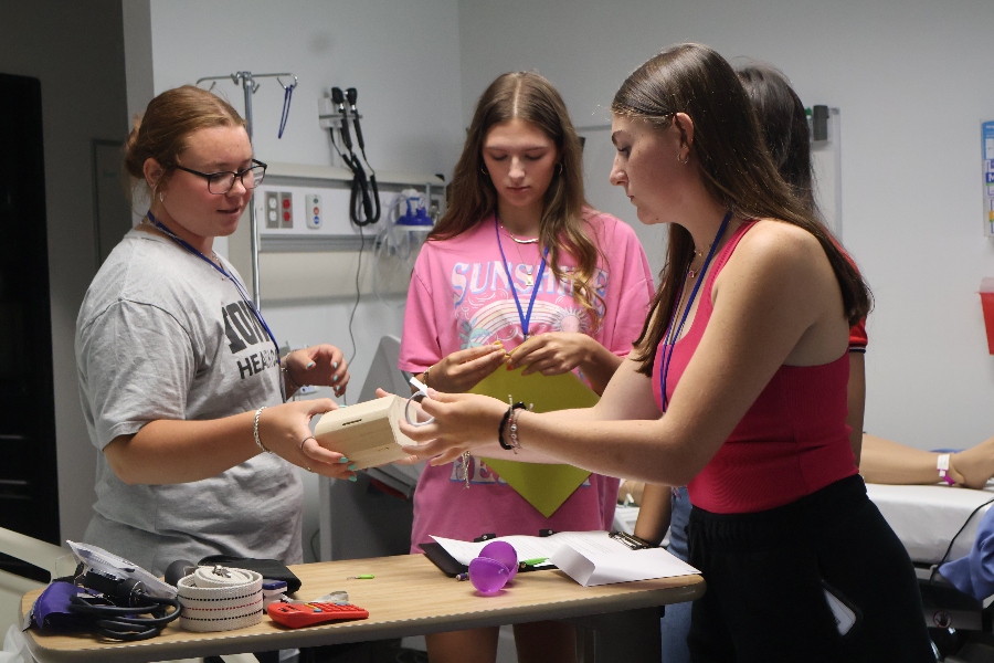 Three high school girls collaborate on a scavenger hunt in a medical room