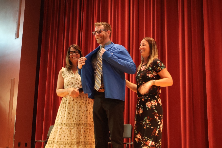 Two OT professors help a student put on a blue coat on stage