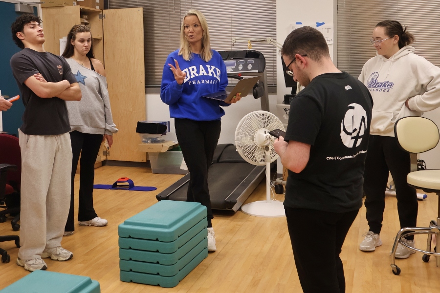 Drake students listen as their professor talks in a lab with exercise equipment