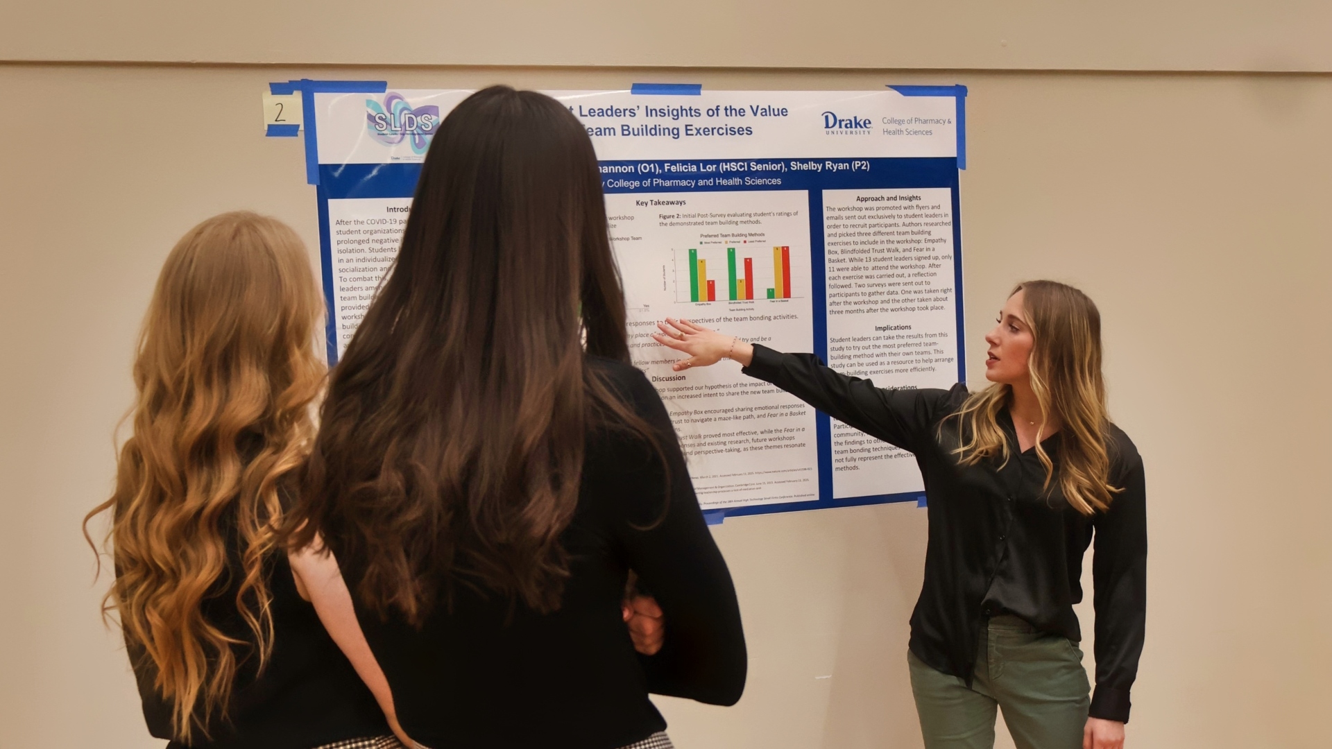 A Drake student in professional dress presents a research poster to two peers