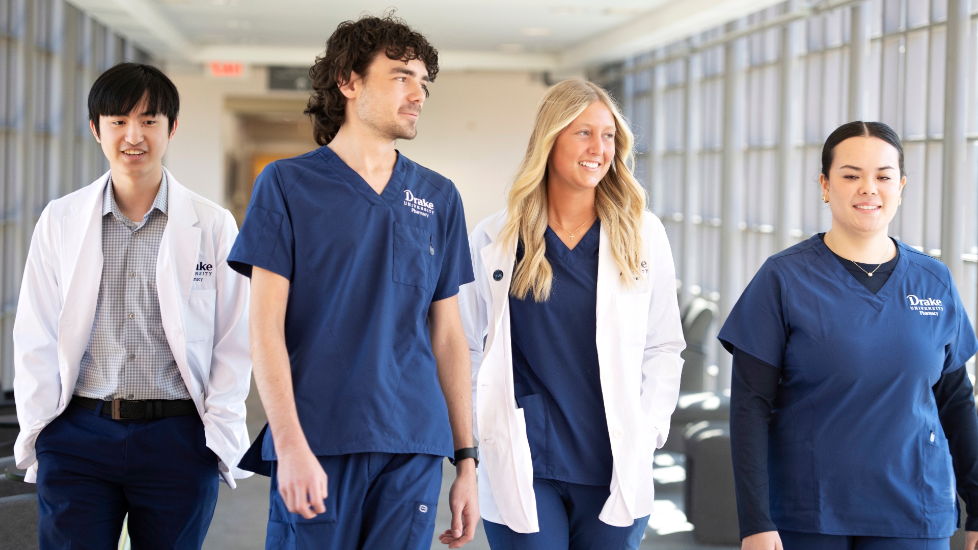 A group of Drake students in white coats and scrubs talk as they walk down a hallway