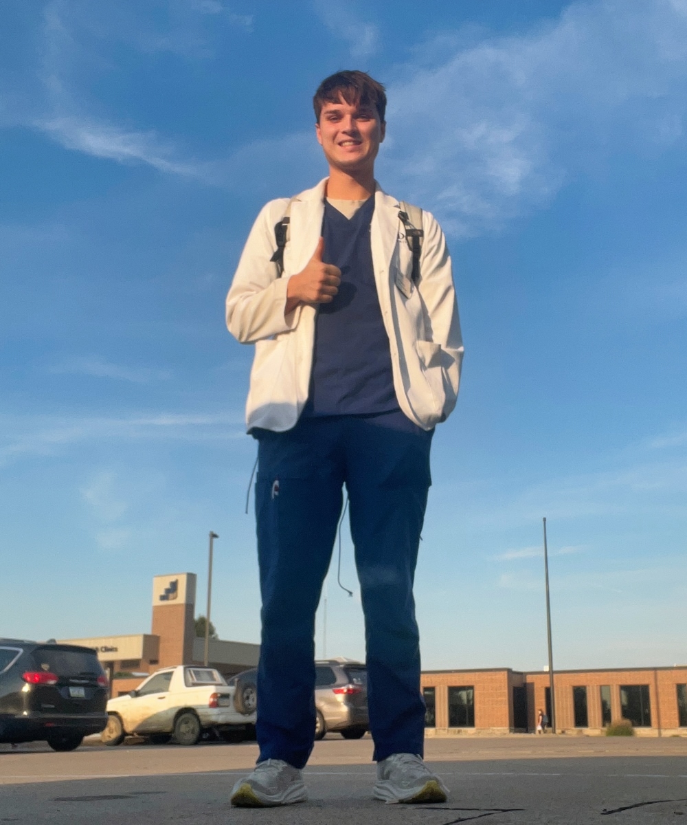 Jack Durman posing with a thumbs up in a parking lot wearing a white coat