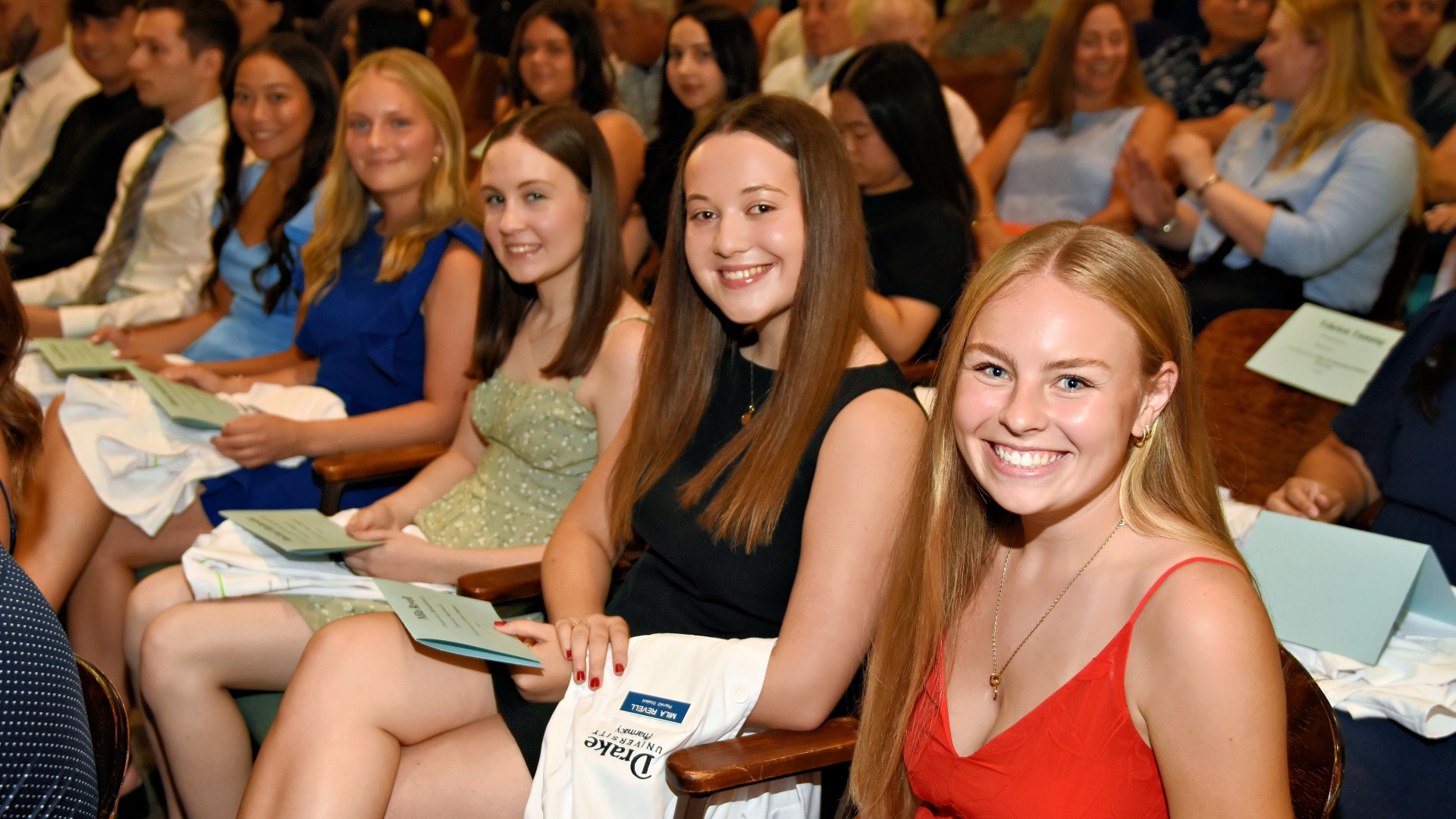 Students smiling with their white coats in their laps before the coating ceremony