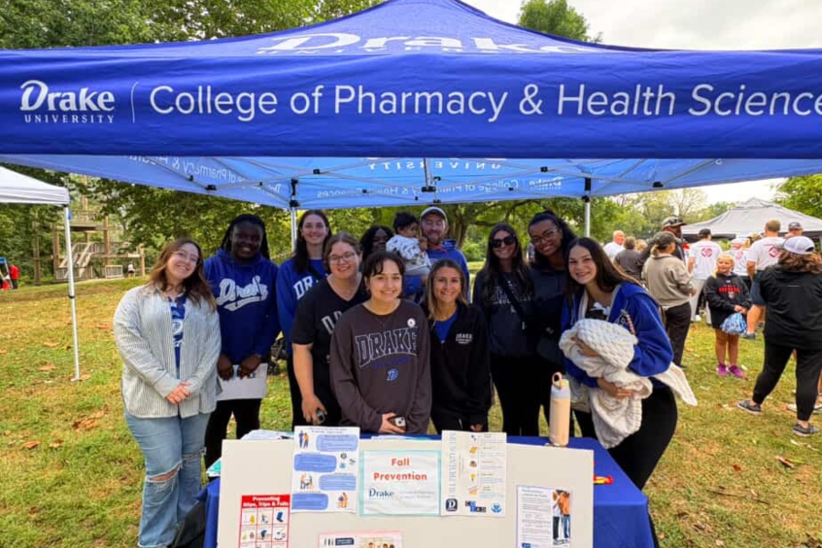 Group of pharmacy and OT students stand under a Drake tent with a fall prevention poster
