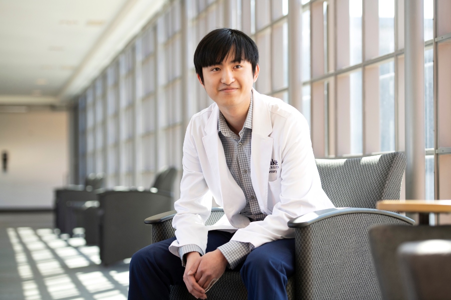A Drake student in a white coat sits in a chair and smiles into the distance