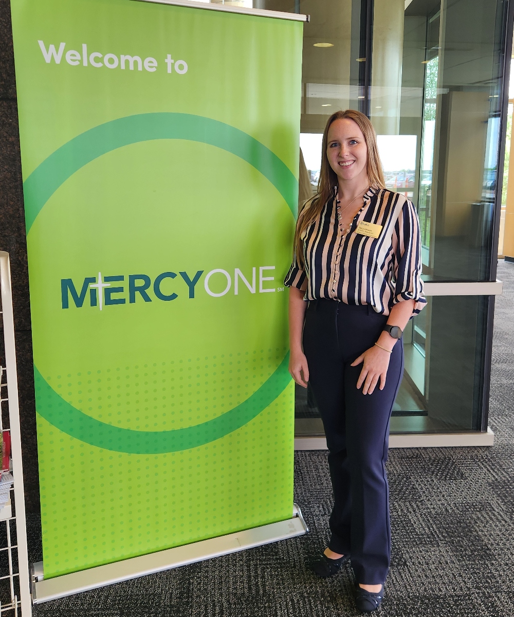 Stacy Johnson standing in front of a Mercy One banner wearing professional clothing and her Drake name tag