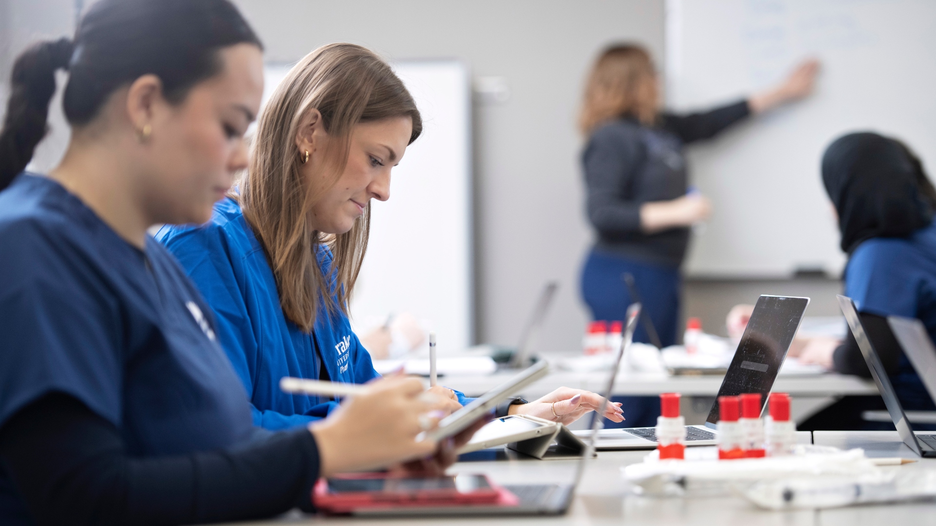 Two pharmacy students take notes in a pharmacy lecture