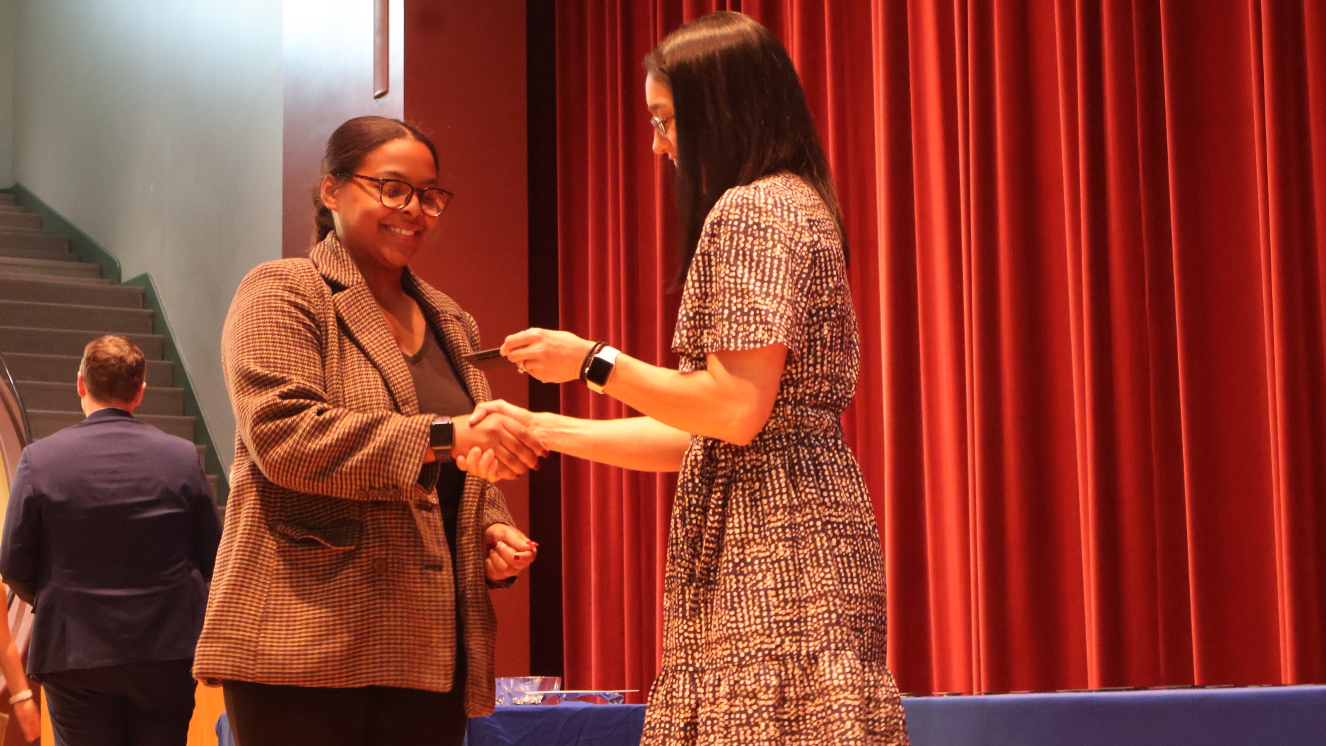 Female student shakes the hand of a professor as she is handed a professional name tag on stage at the pinning ceremony
