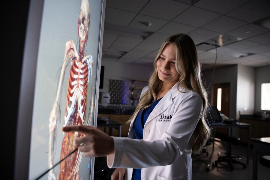 A female student in a white coat examines a skeleton using digital anatomy equipment