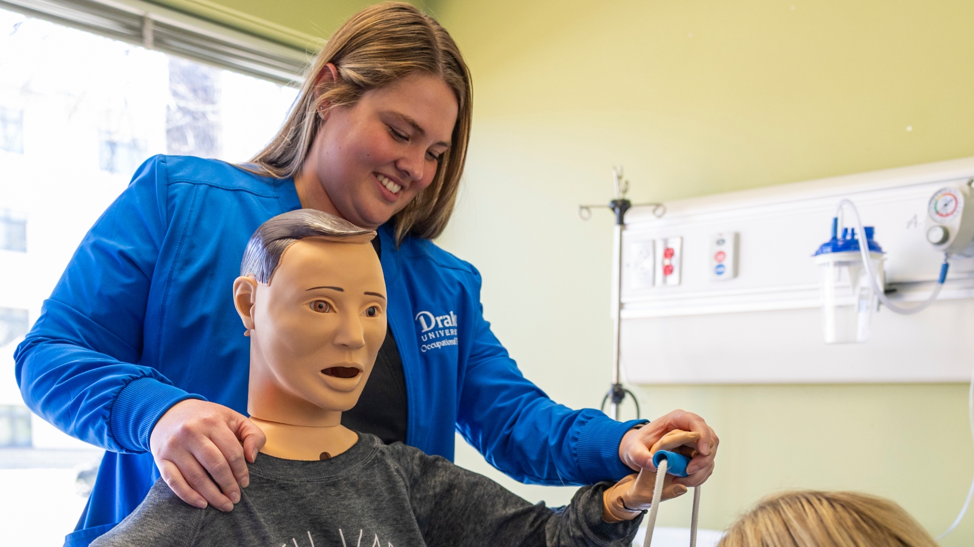 Occupational therapy student smiling and moving the limbs of a mannequin 