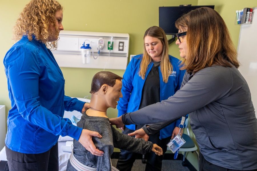 Two Drake students help a professor move the limbs of a mannequin
