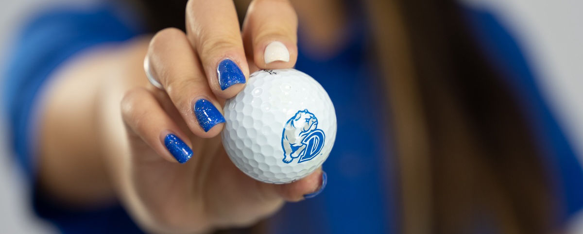 Woman holding a Drake Athletics Golf Ball up to the camera with blue and white painted nails.