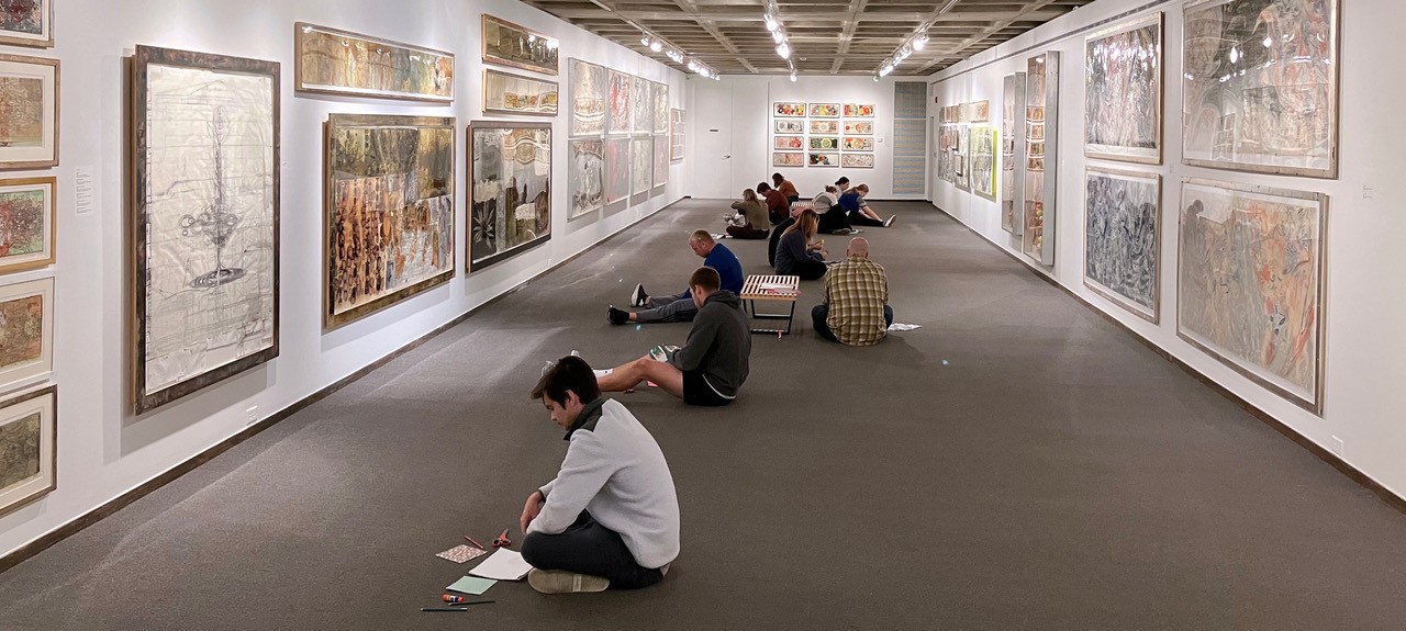 Group of people sitting on the ground in the Anderson Gallery while looking at the artwork.