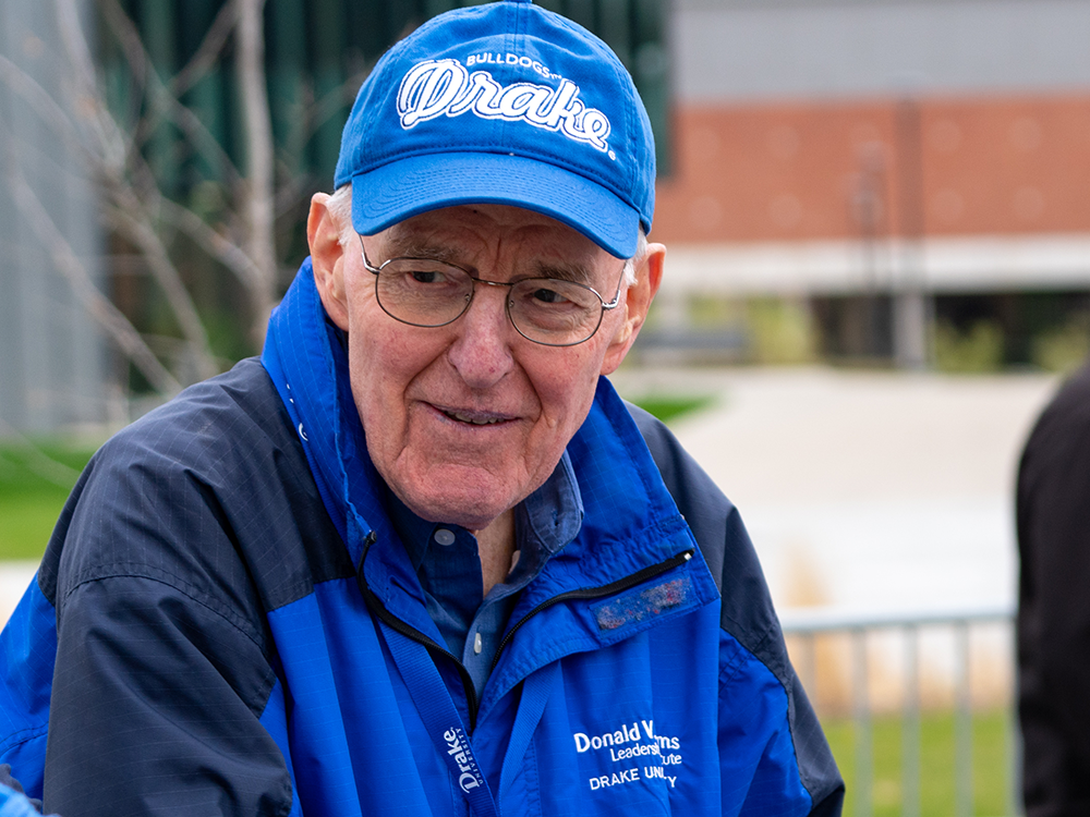 Donald V. Adams at a Drake University Alumni event wearing a Drake Bulldogs hat and a Donald V. Adams Institute jacket.