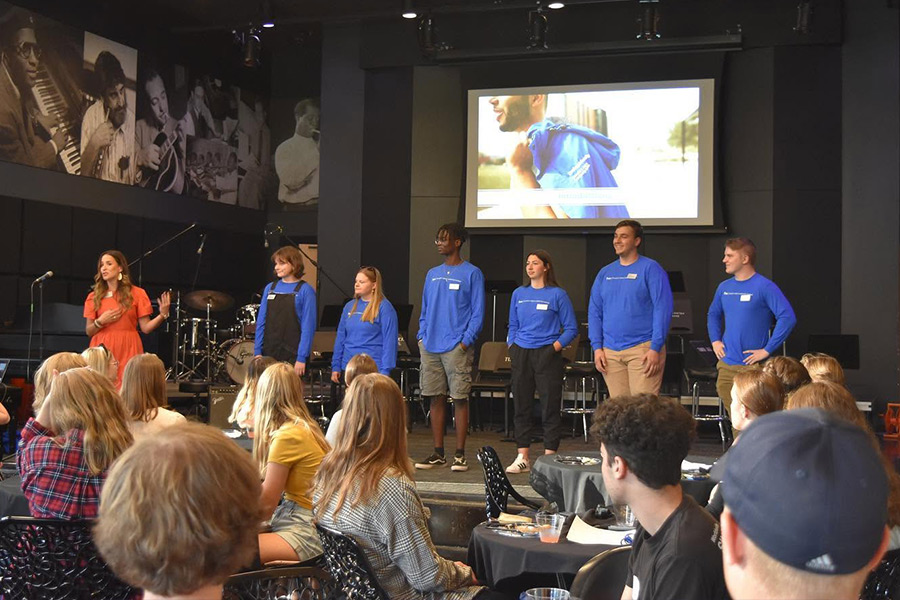 Kristin Economos standing with 6 Leadership Institute students on stage while talking to a room full of people in the Turner Jazz Center.