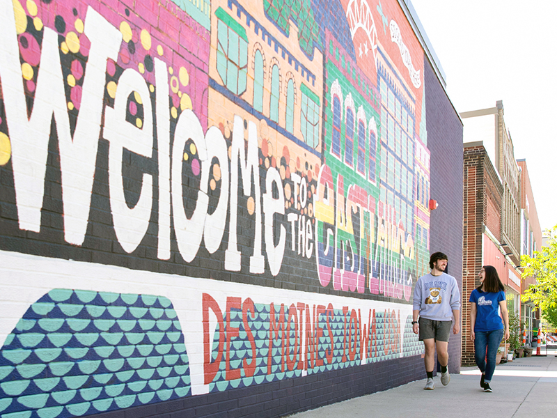 Two Drake students walk by a colorful mural that welcomes them to Des Moines