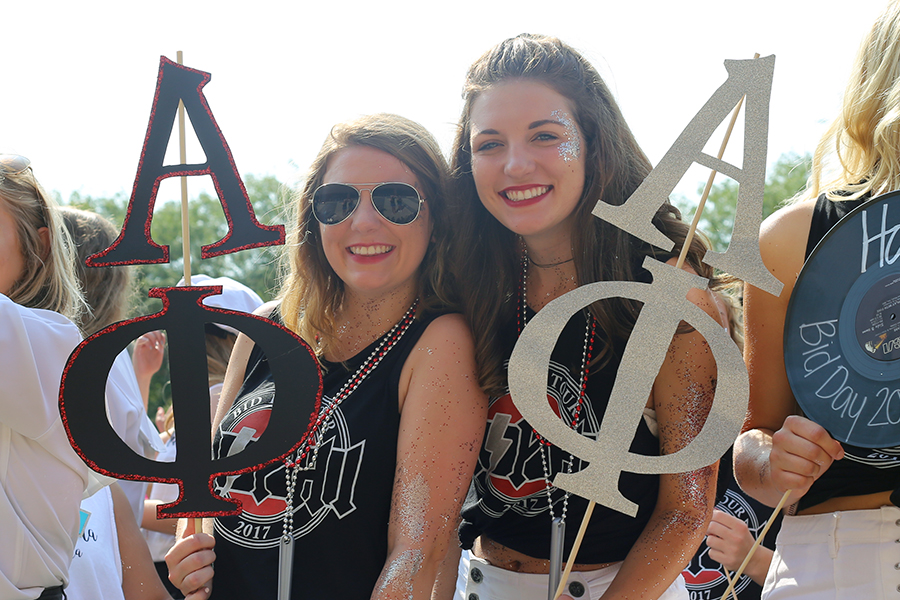 Two smiling Drake students, one in sunglasses and the other with silver glitter face paint, pose with their Greek organization's letters during an event
