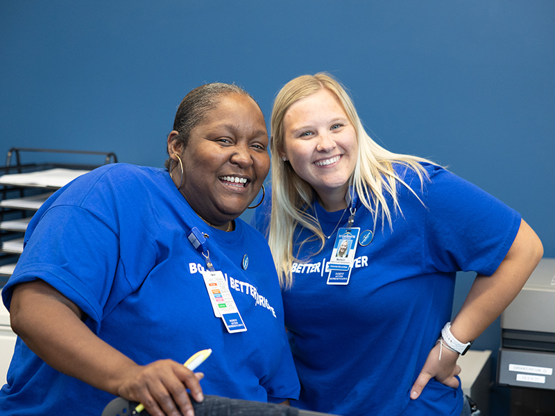 Two workers for Drake University's Counseling Center in blue T-shirts and ID lanyards smile for the camera