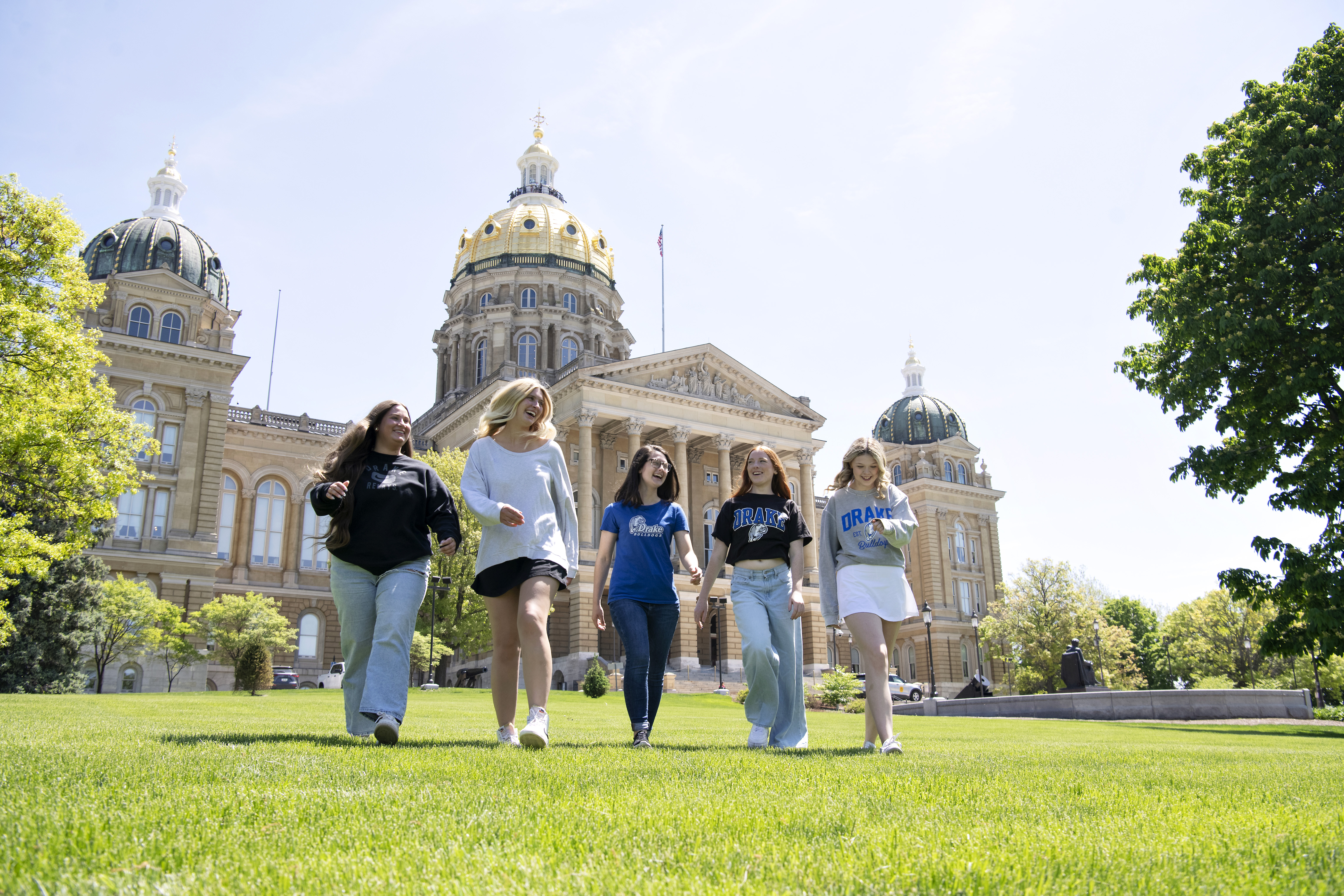 A group of Drake students, many wearing shirts that sport the school's logo, walk on the grass in front of the Iowa State Capitol building