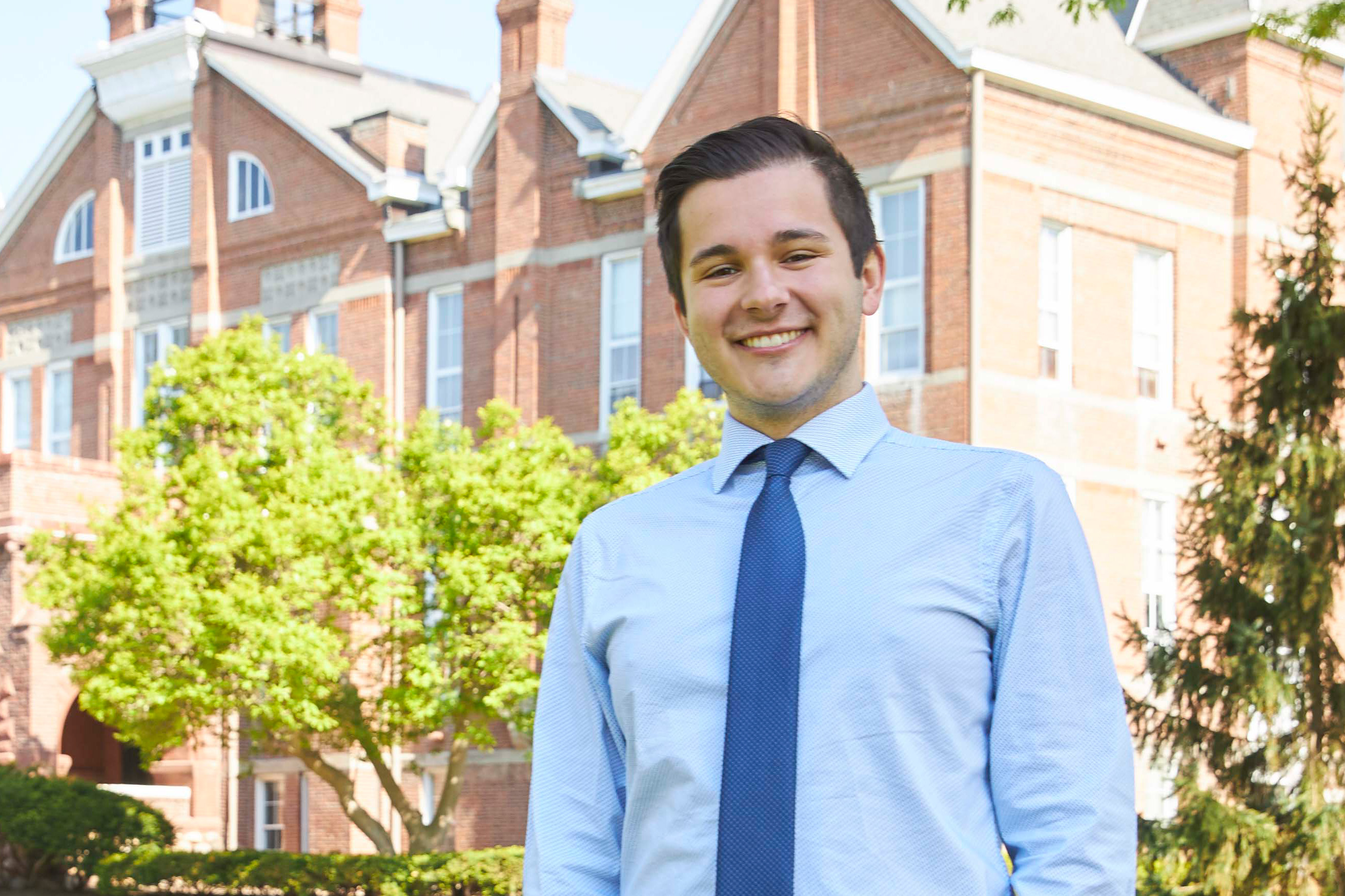 A student in a blue dress shirt and tie smiles at the camera