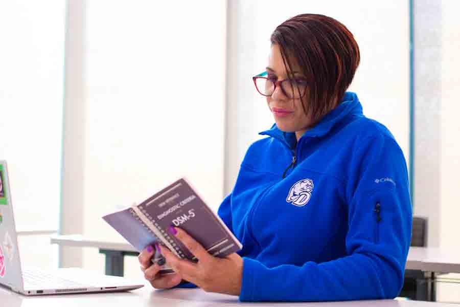 A student in a Blue Drake pullover sits at a table reading a book