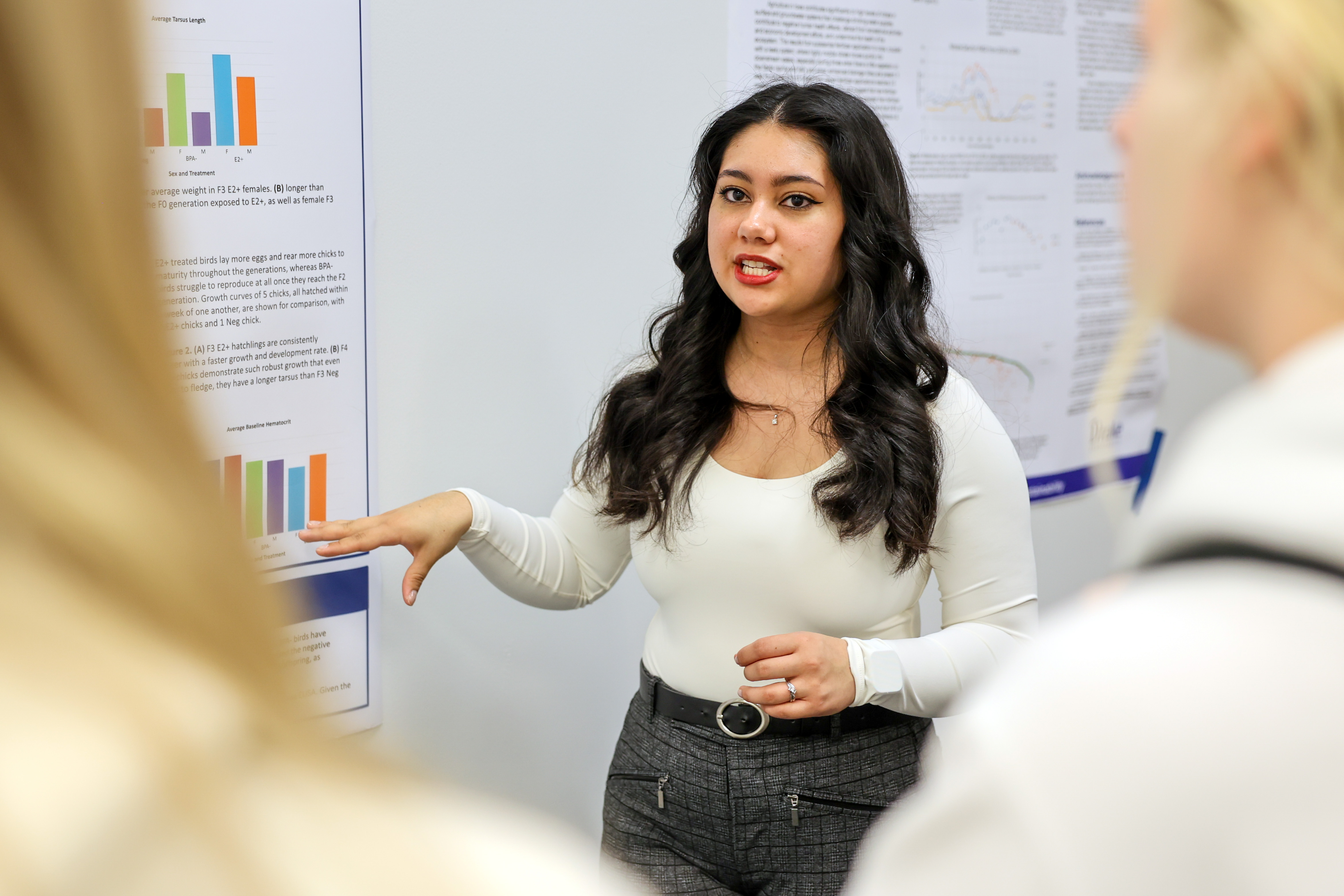 A student stands in front of a research poster while speaking