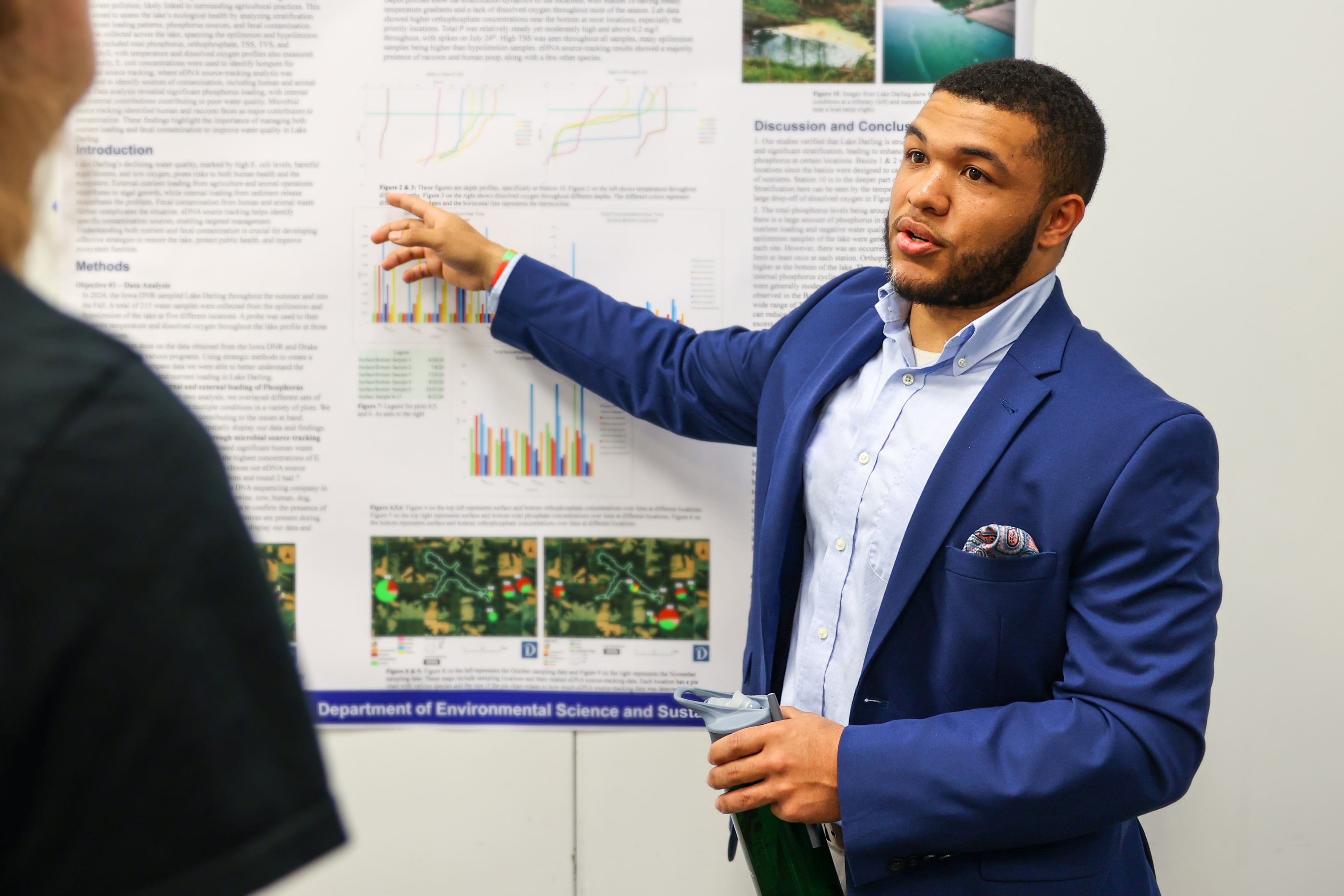 A student in business attire points to a poster while presenting