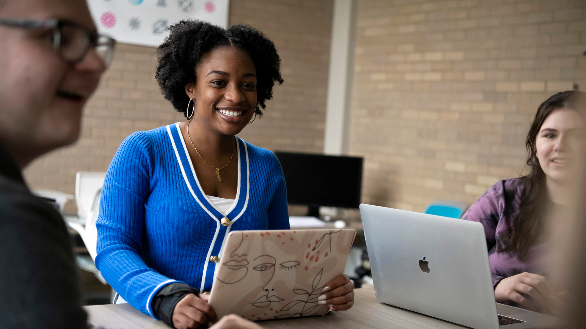 Students sitting around a table with laptops while smiling