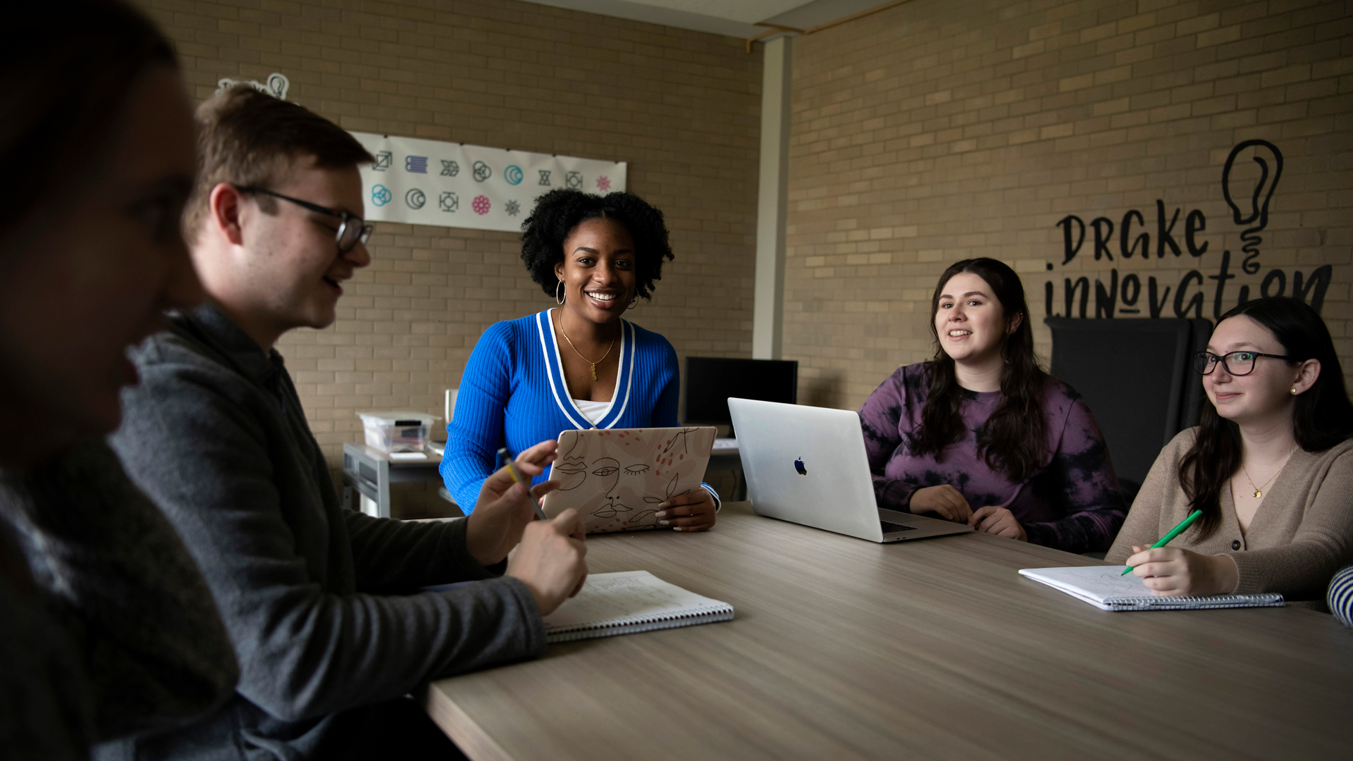 A group of students sit around a table with laptops and notebooks