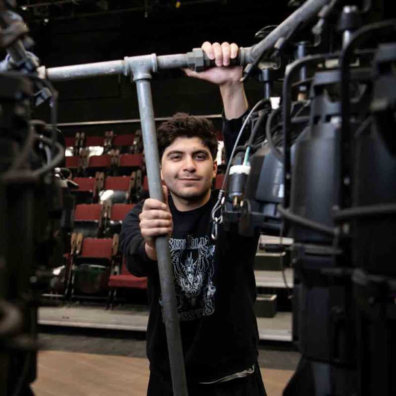 A smiling student holds onto metal piping that is part of a stage setup