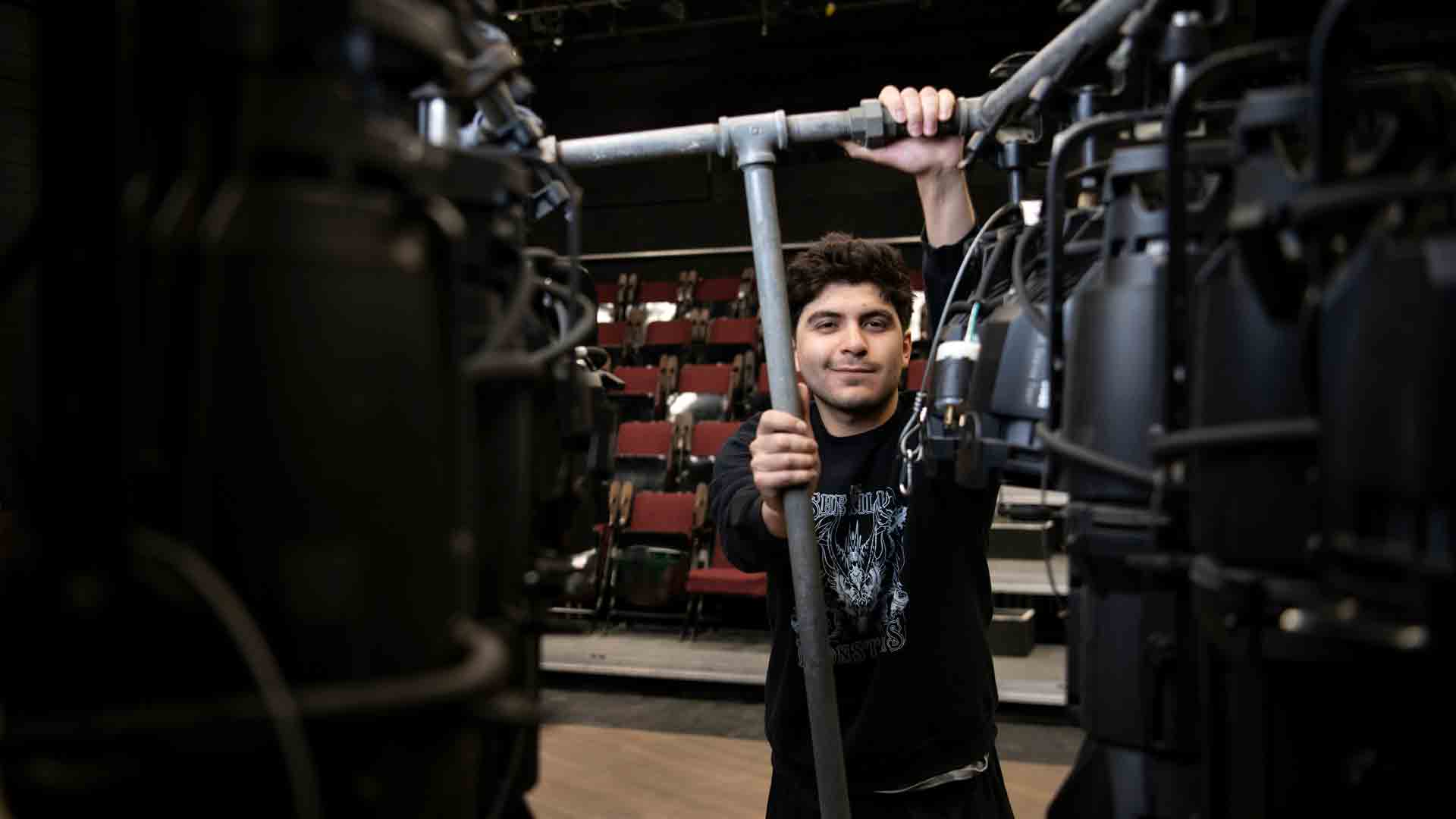 A student smiles at the camera while holding piping for stage lighting
