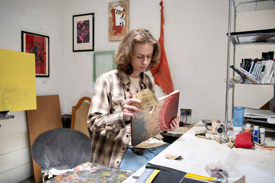 A student sands the edges of a wood art piece in an art studio