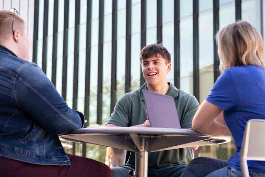 A group of students sit at a table smiling at each other