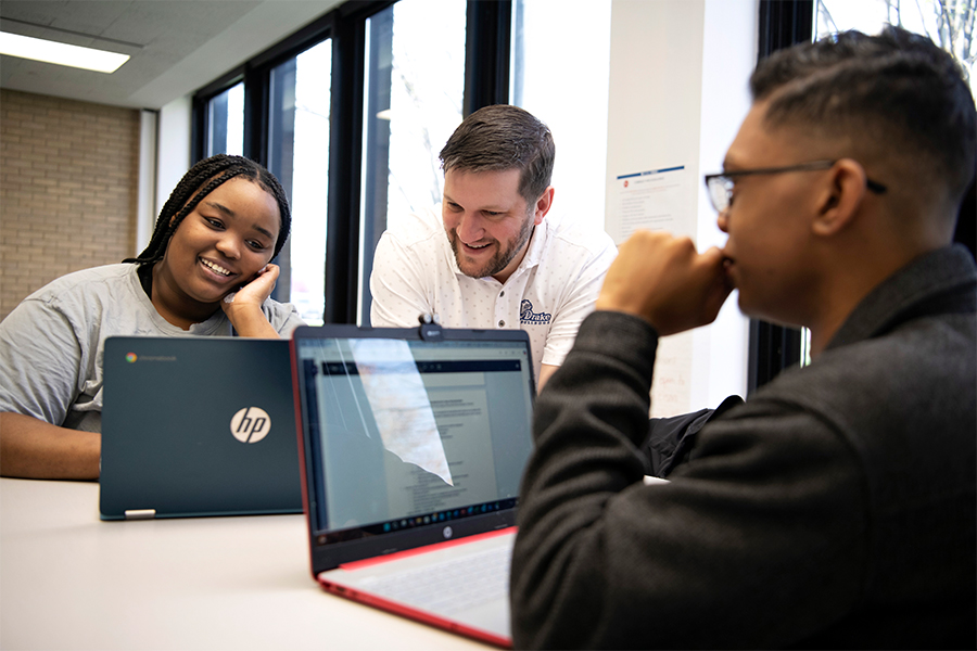 Two students in Drake's A.A. in Business, Organization, and Professional Studies program learn about J-Term trips from a faculty member