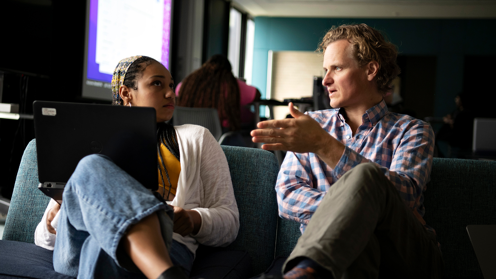 A faculty member holds a discussion with a student in Drake's A.A. in Integrated Arts, Sciences, and Humanities program, both sitting on a common area couch