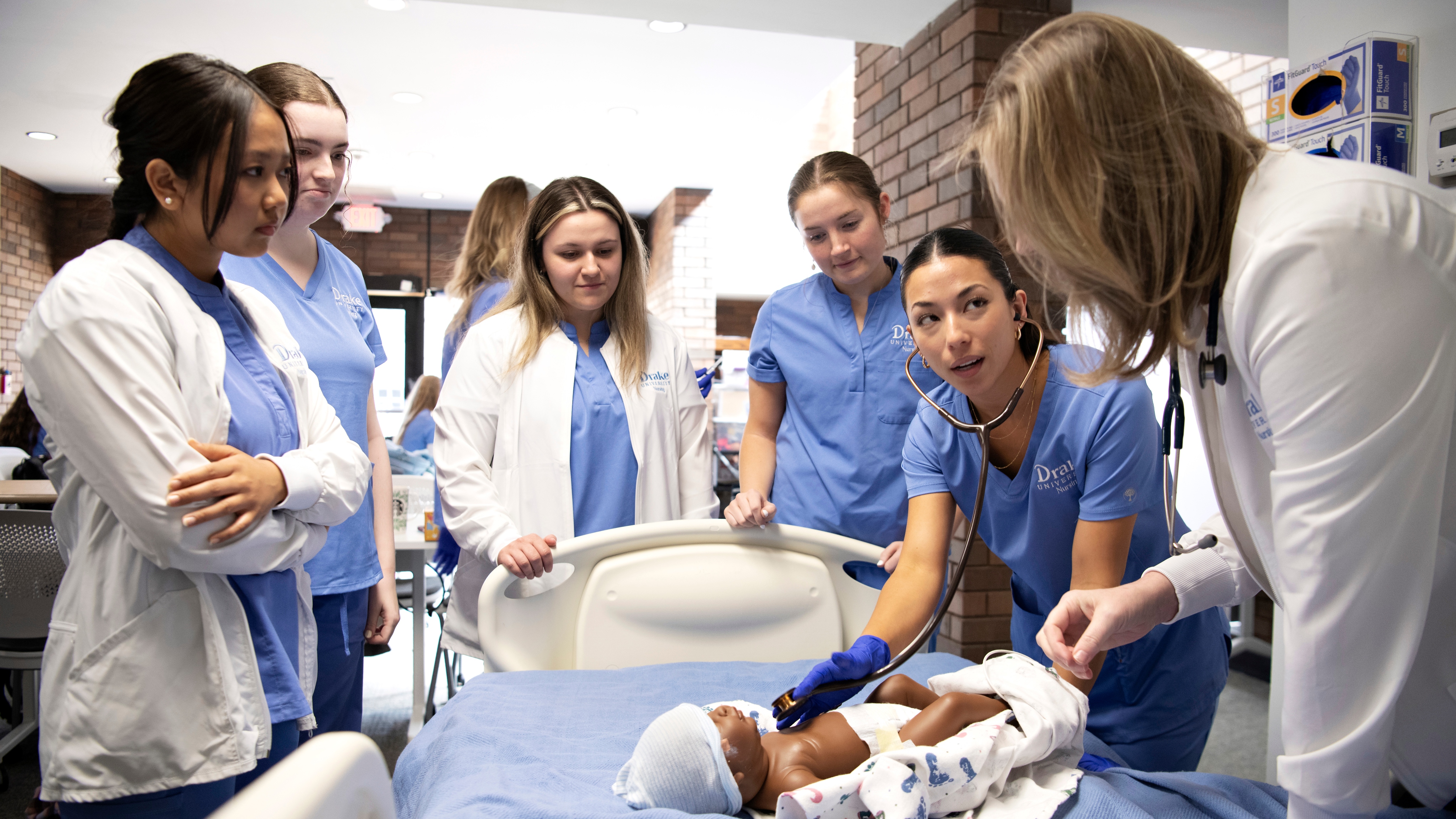 Drake University Nursing students practice taking vitals on an infant mannequin with a stethoscope in a simulation lab