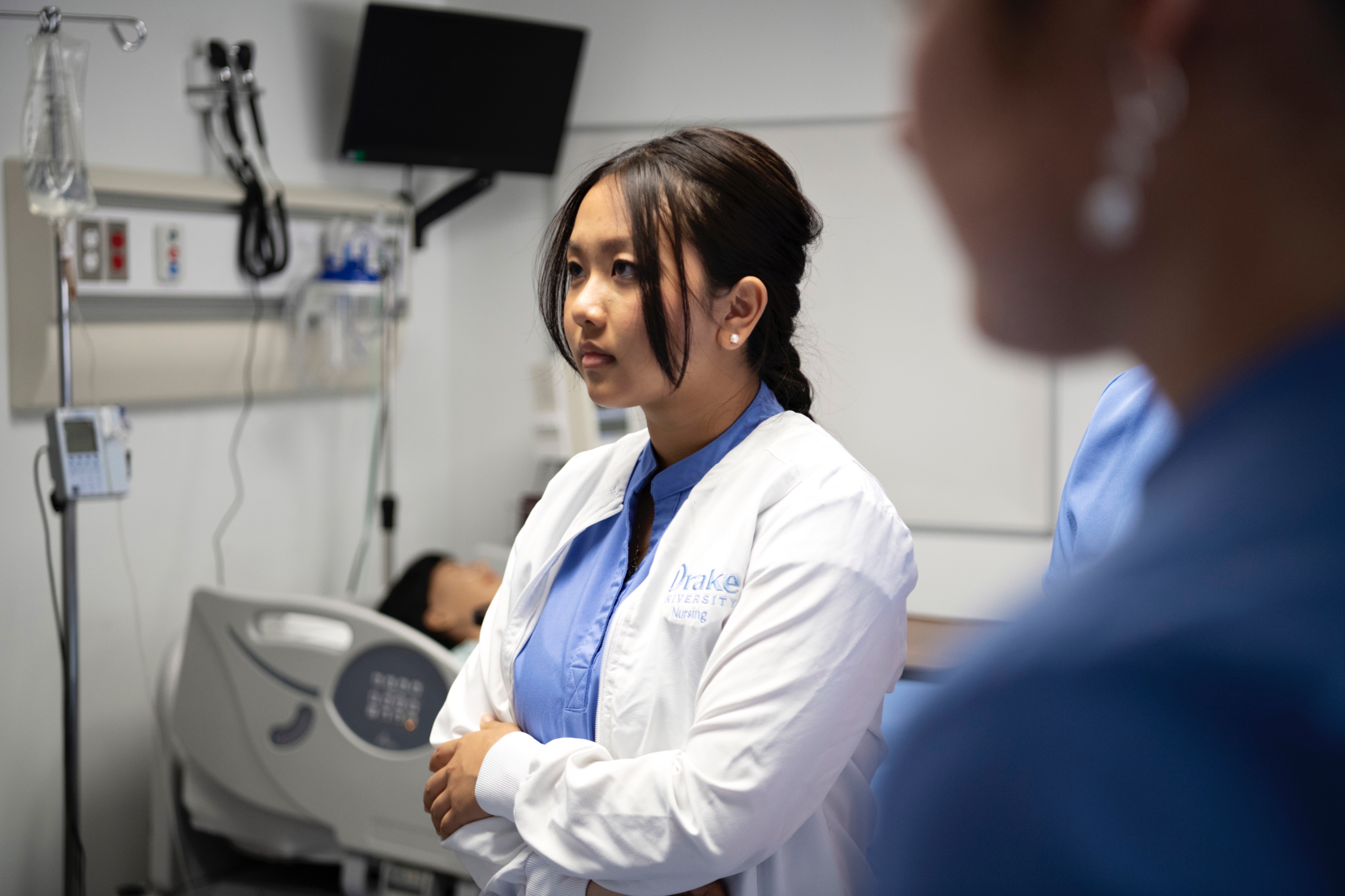 A Drake ABSN student in a white jacket and blue shirt concentrates in a campus simulation lab