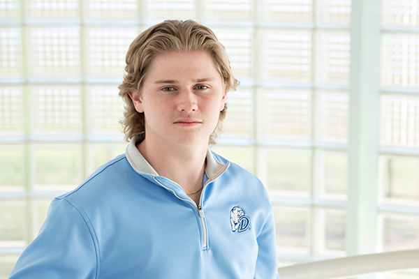 A Drake Accounting student in a blue quarter-zip school pullover ponders a question in a room with glass brick walls