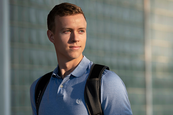 A Drake Actuarial Science major wearing  a blue polo shirt and backpack turns to the right