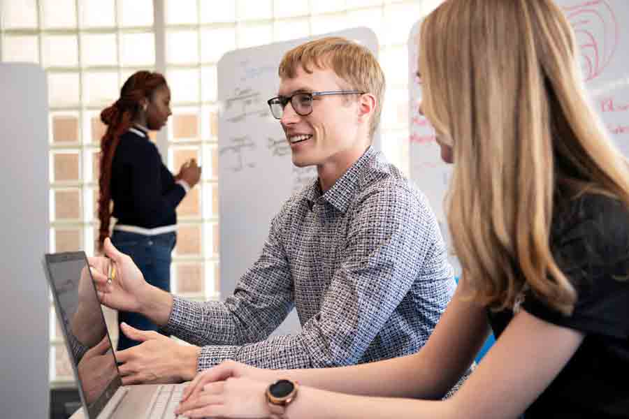 Two students have a discussion around a laptop in Drake's Insurance Innovation Lab, while another student writes ideas onto a large whiteboard in the background.
