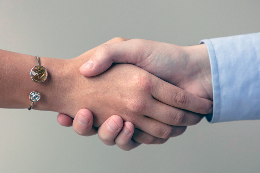 Two hands shake, with one wearing a bracelet and another with a visible blue shirt cuff