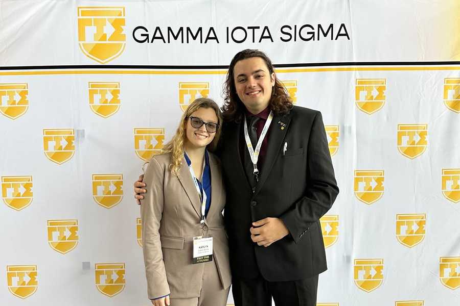 Two Drake Actuarial Science Minors stand in front of signage for the Gamma Iota Sigma fraternity
