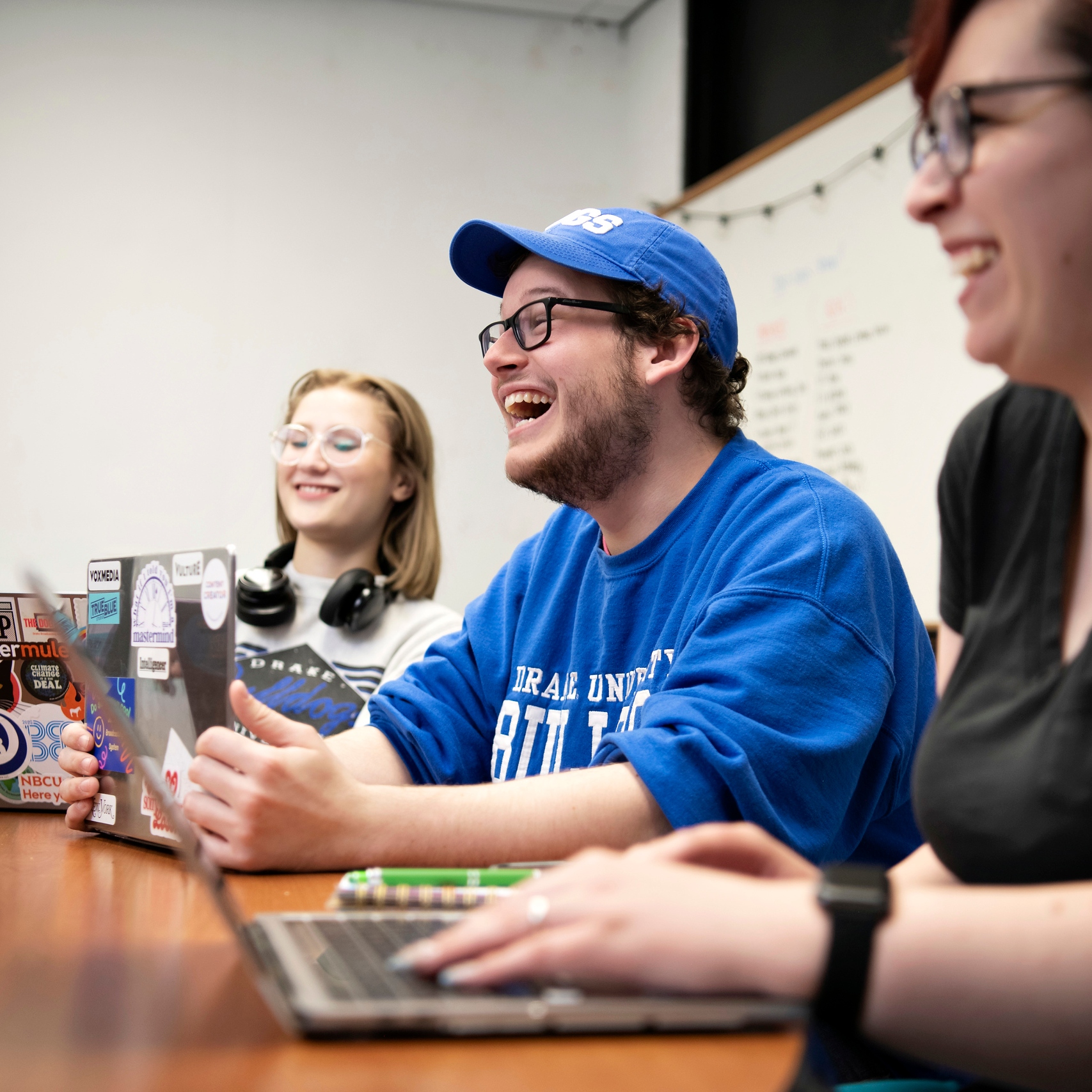 A smiling group of Advertising Majors at Drake converse around a table while using their laptops