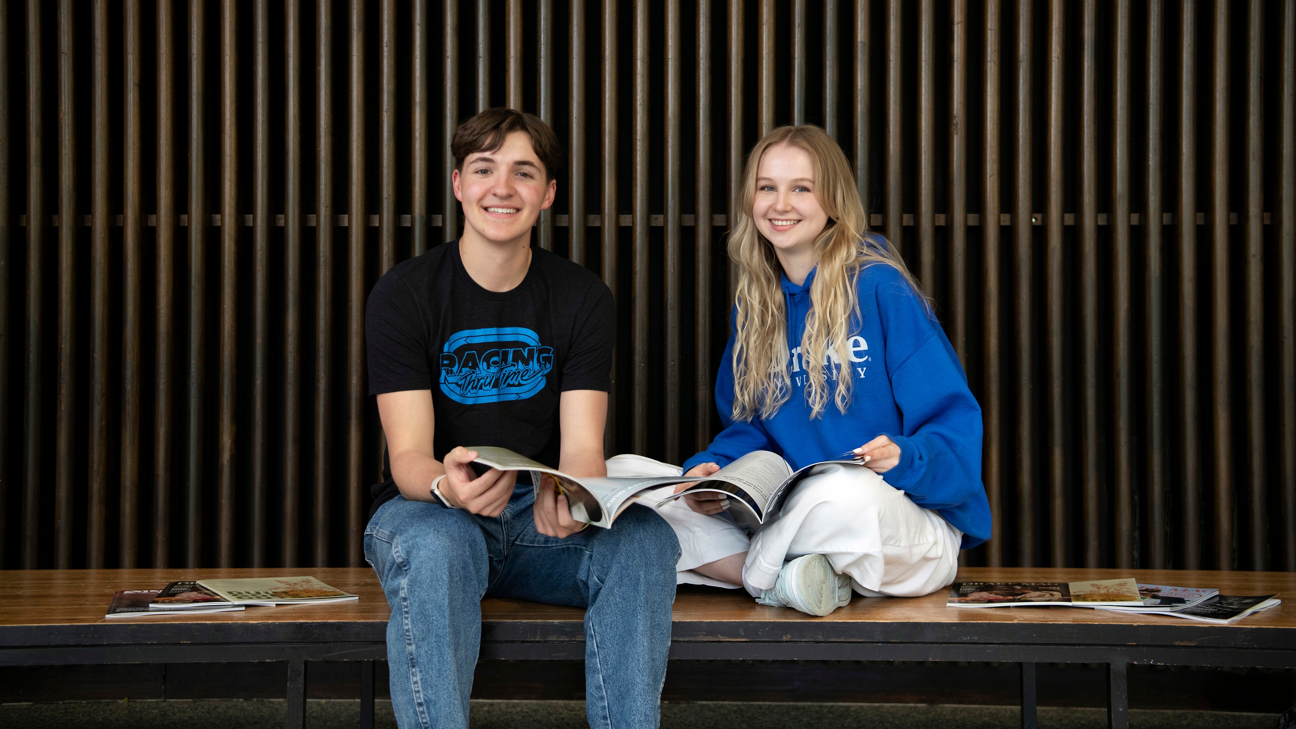 Two Advertising Majors from Drake University read magazines on a bench in a common area with a ridged wall