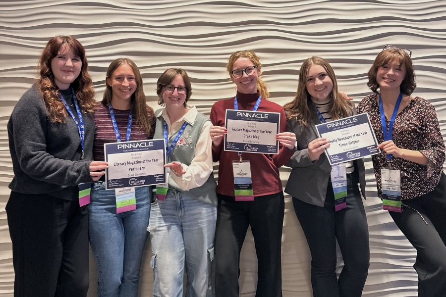 A group of Drake University Advertising Majors proudly display award certificates as they stand in front of a wave-textured wall