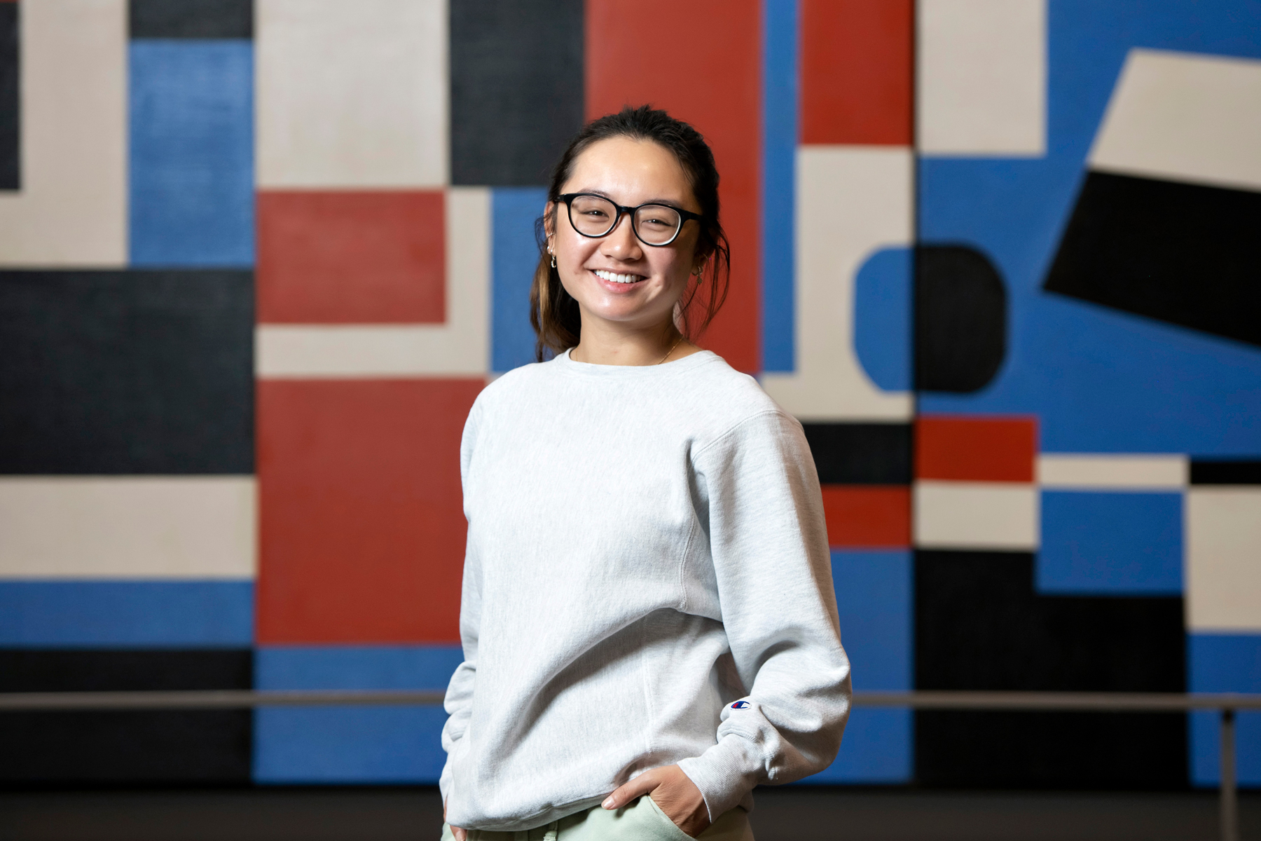 A Drake Art History student smiles and stands in front of a wall with a colorful geometric pattern