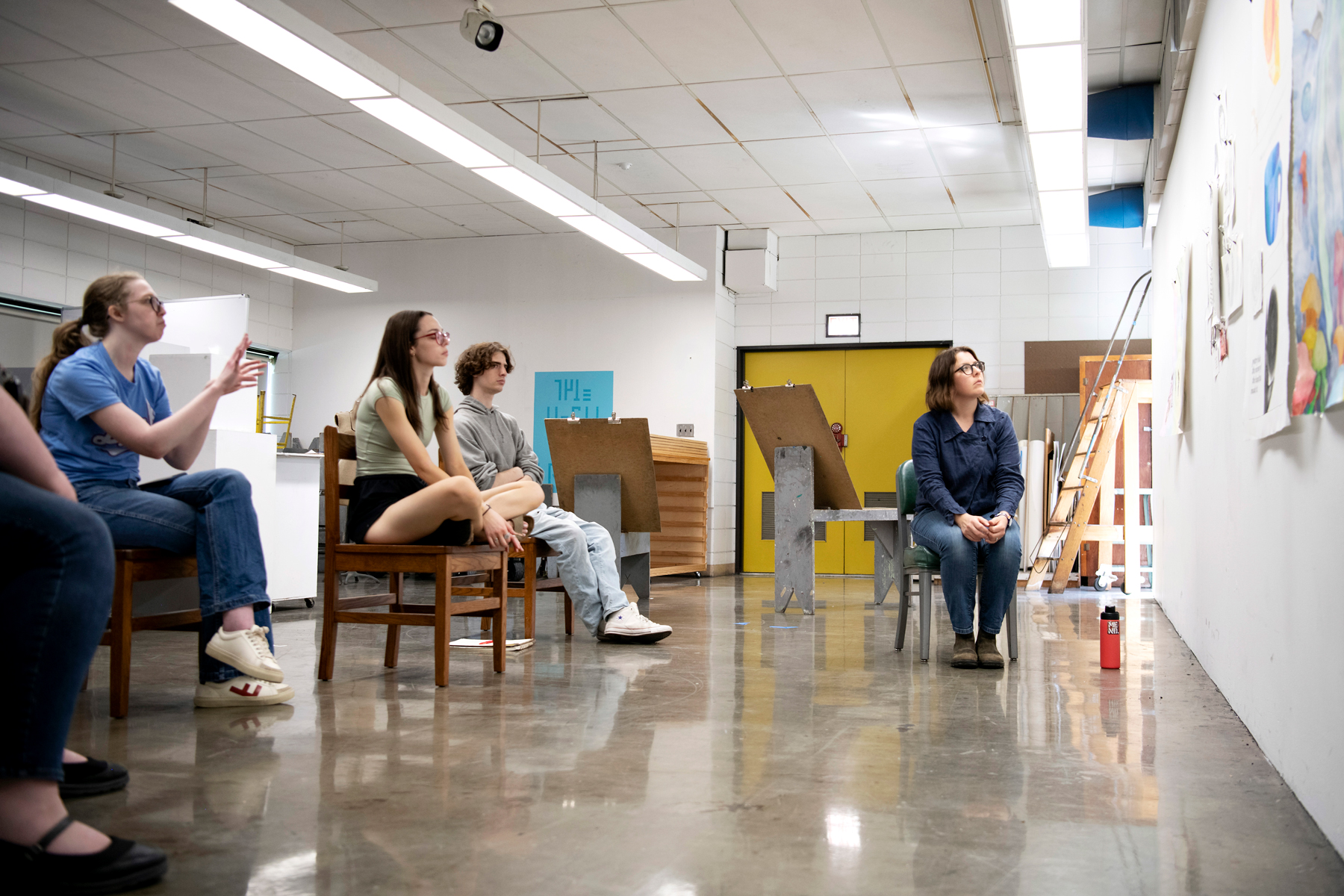 In a campus studio, Drake Art History students discuss works presented on a wall with their professor